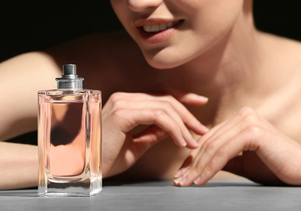 Beautiful young woman with bottle of perfume on dark background,